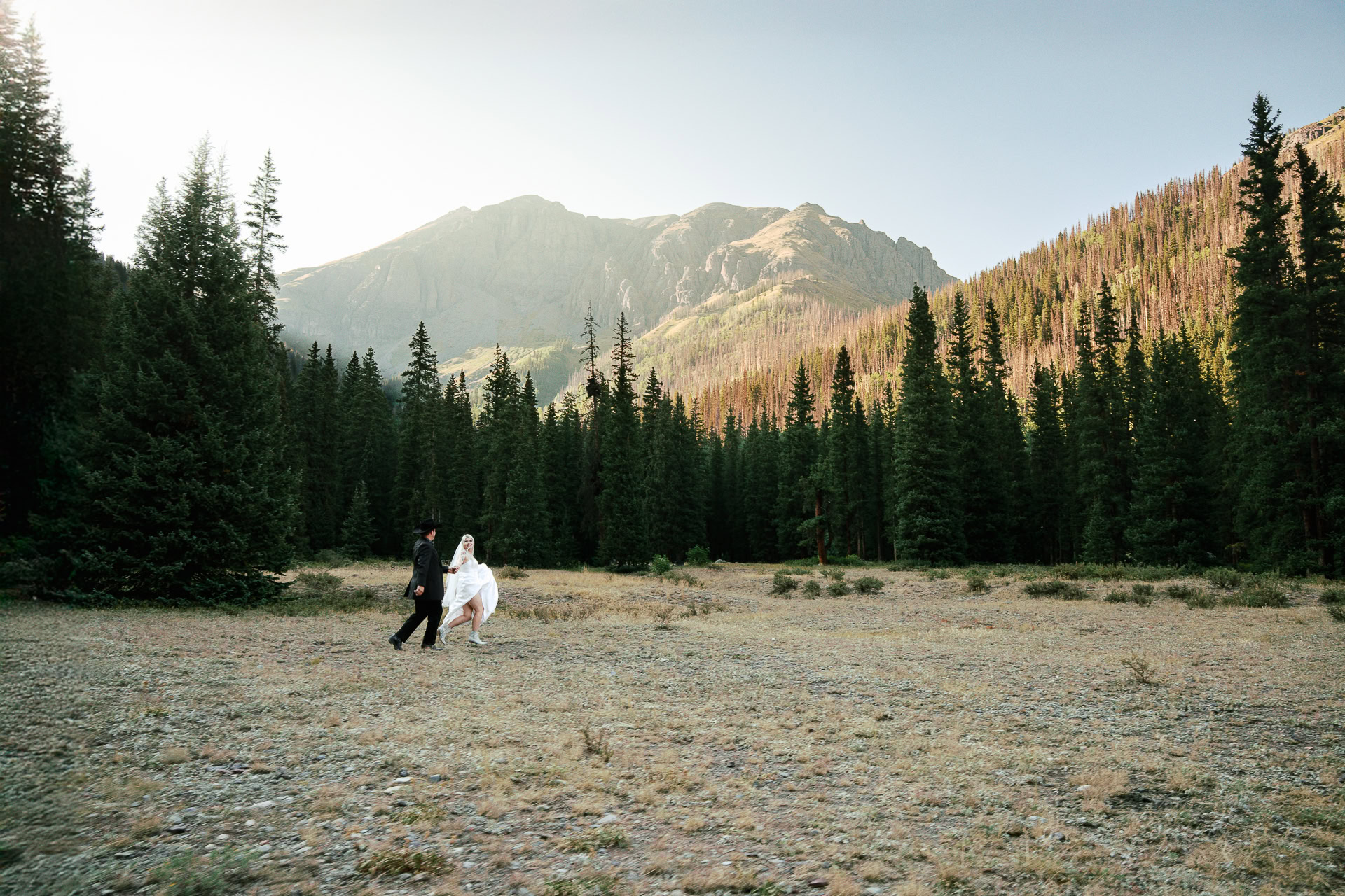 San Juan Mountains elopement photo of couple playfully running hand in hand in front of dramatic peaks