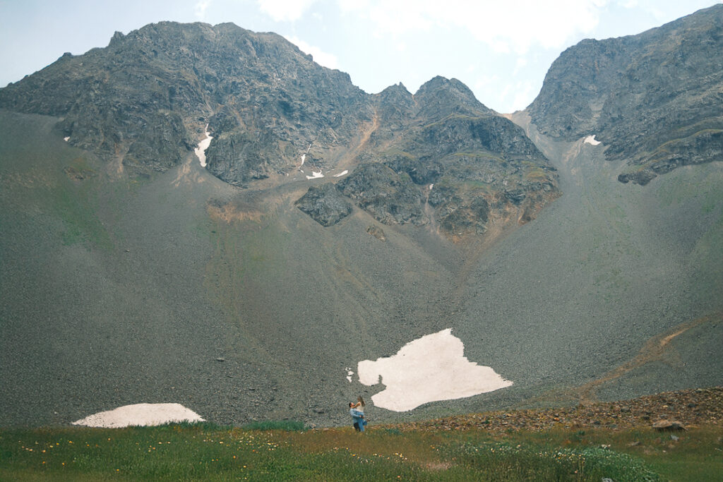 Colorado mountain elopement in the San Juan Mountains with a couple embracing in a high alpine meadow surrounded by dramatic rocky peaks and snow patches.