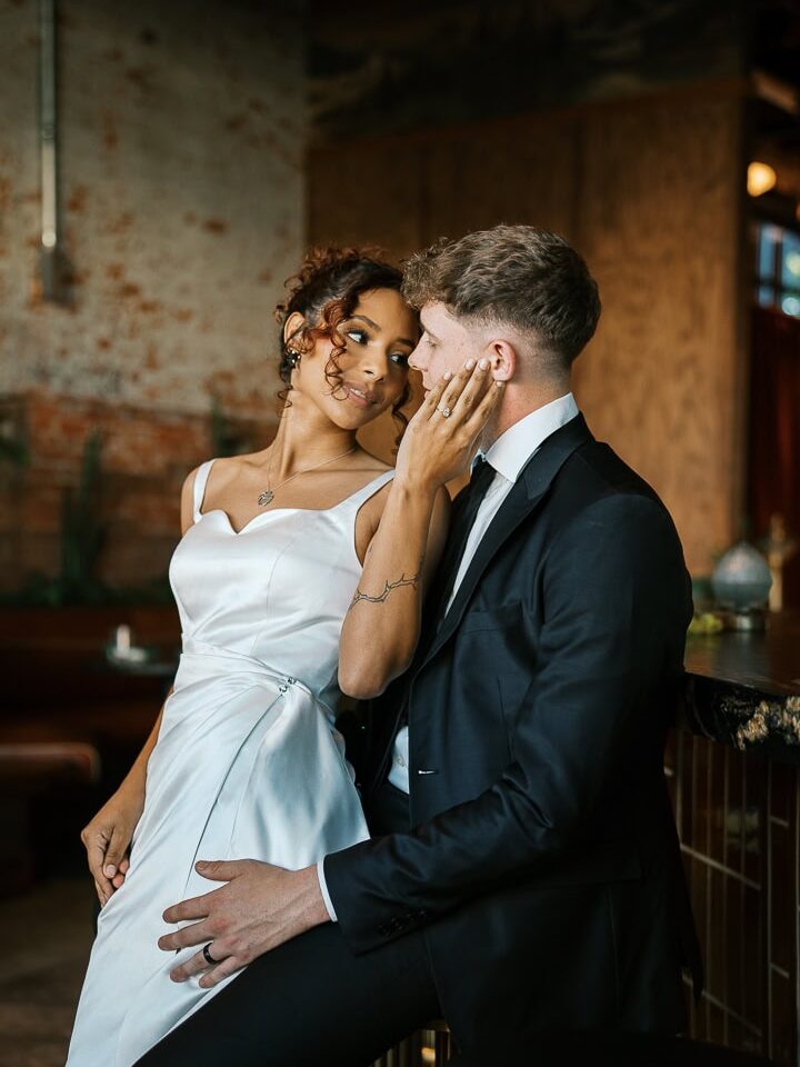 Waco wedding photographer captures romantic moment at Hotel Herringbone — stylish couple in a modern, industrial space with the bride in a satin gown and the groom in a black suit sharing an intimate pose.